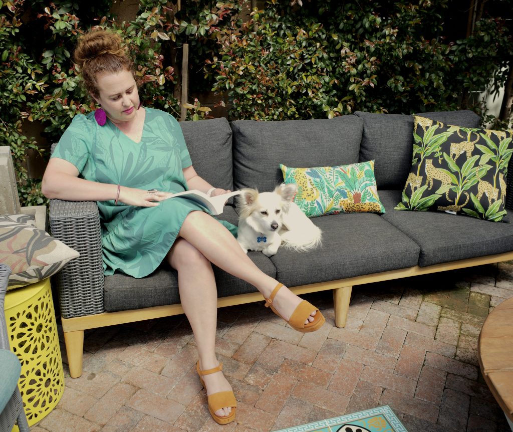Woman in green dress sitting on sofa outside with white dog.