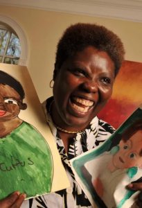 Black woman holding up two paintings, smiling.