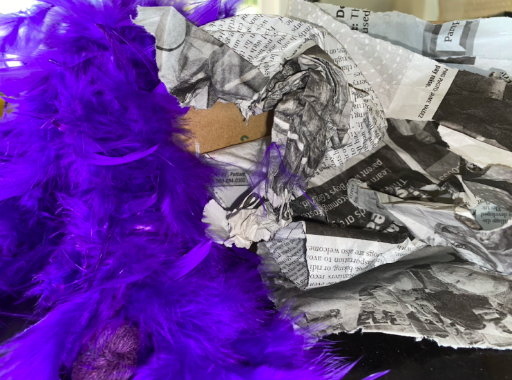 crumbled paper and purple feather boa on side of box.